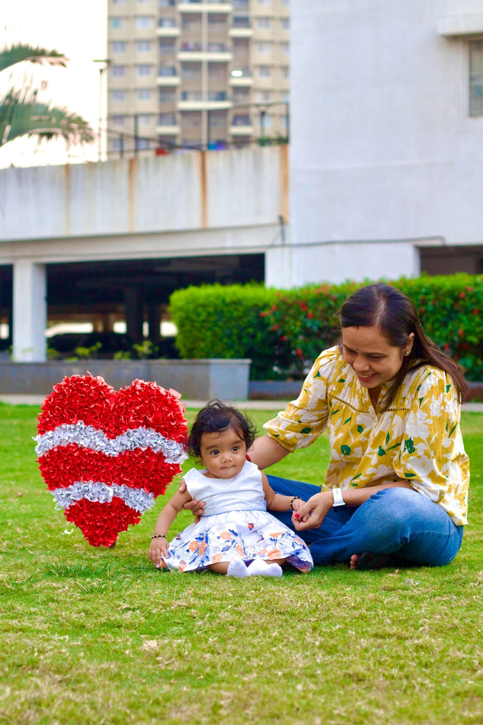 Happy mother and baby enjoying outdoor time at park with decorative heart in Pune, India.